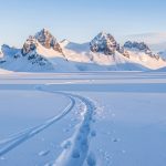 Vue hivernale du plateau enneigé de Solaison, avec des traces de raquettes et les sommets du Bargy en arrière-plan sous une douce lumière matinale.