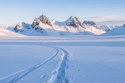 Vue hivernale du plateau enneigé de Solaison, avec des traces de raquettes et les sommets du Bargy en arrière-plan sous une douce lumière matinale.