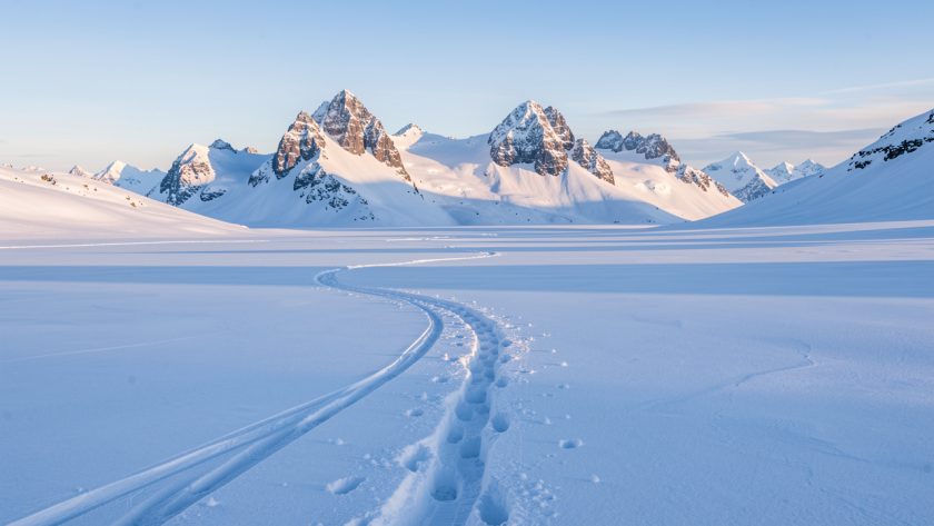 Vue hivernale du plateau enneigé de Solaison, avec des traces de raquettes et les sommets du Bargy en arrière-plan sous une douce lumière matinale.