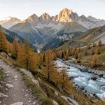 Vue panoramique de la vallée du Vénéon depuis Saint-Christophe-en-Oisans, avec un sentier de randonnée, des mélèzes, un torrent et les sommets des Écrins baignés par la lumière matinale.